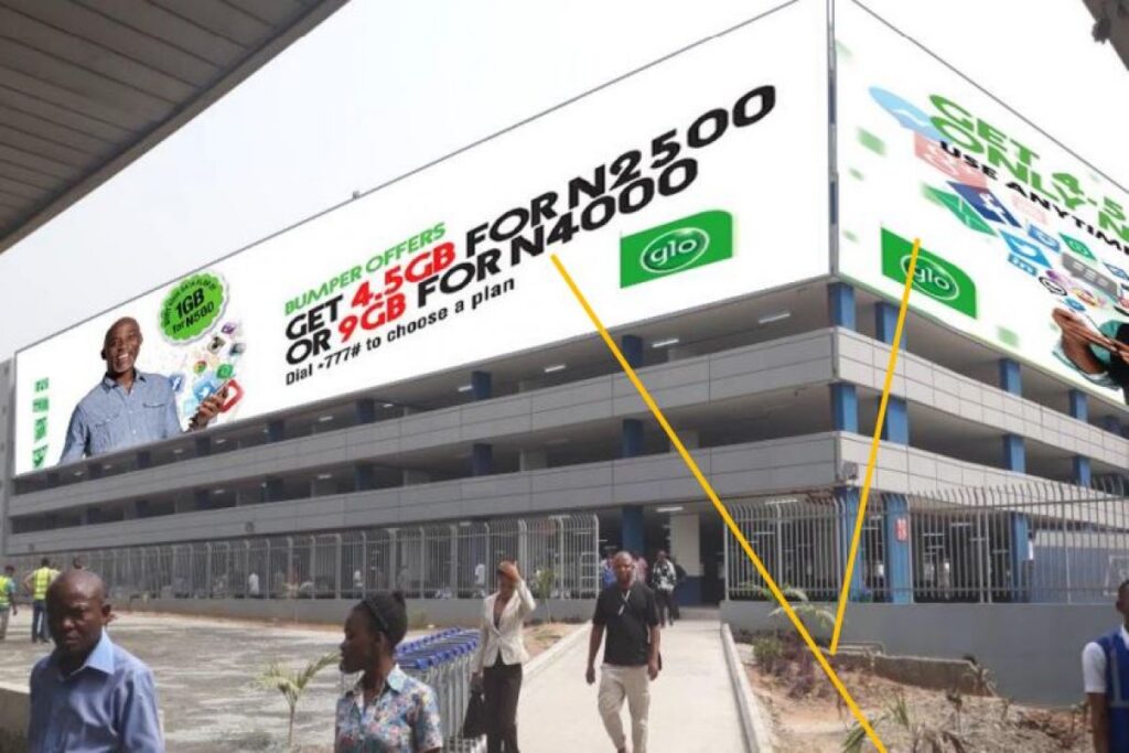 Billboards at Murtala Muhammed showcasing Glo advertising display at the airport with pedestrians walking below.